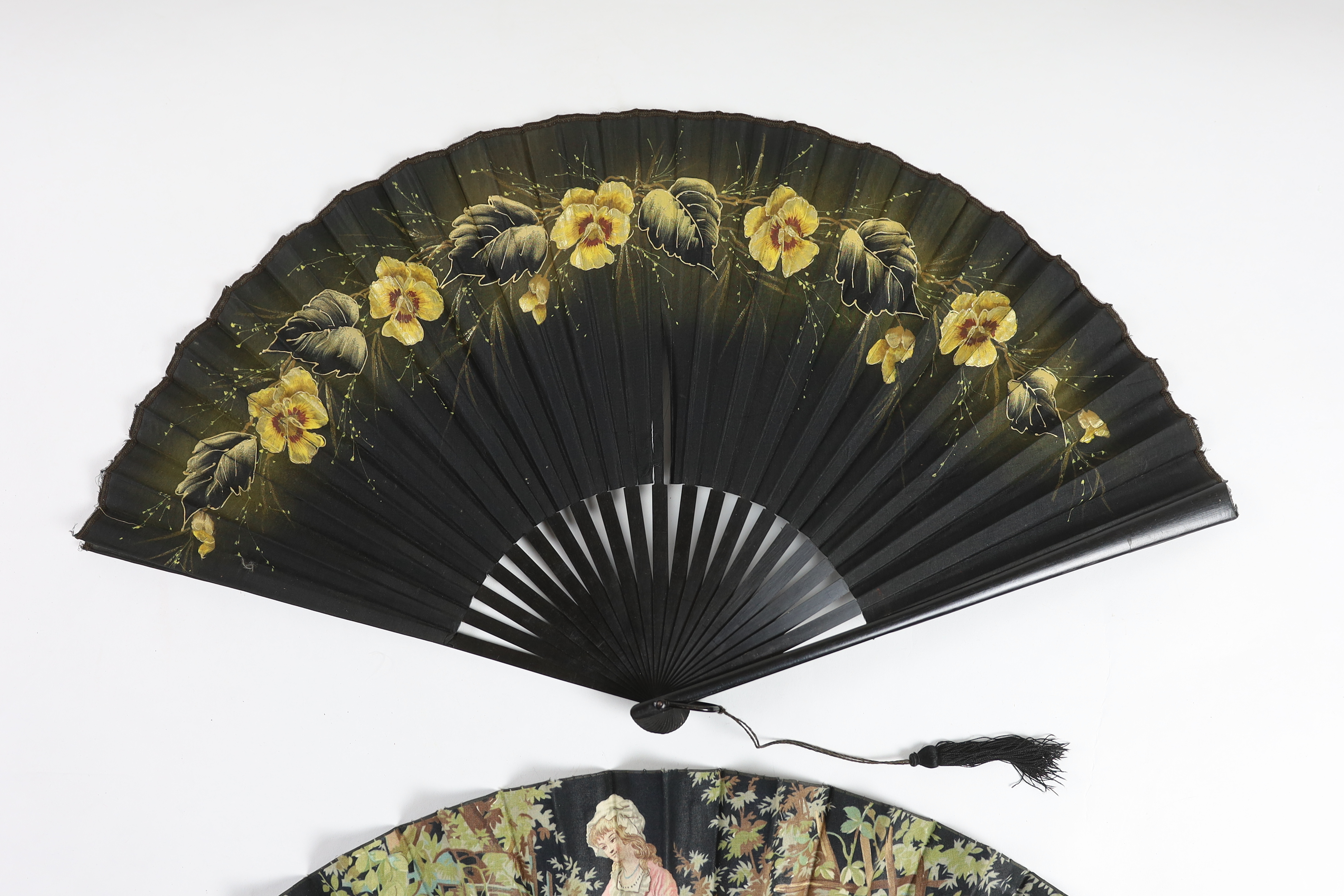 Two early 20th century ebony fans, one cotton leaf, the other hand painted pansies on a fine a silk leaf